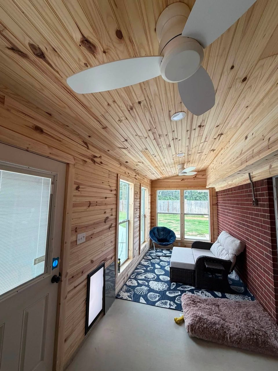 Wood-lined enclosed room with ceiling fans and large windows.