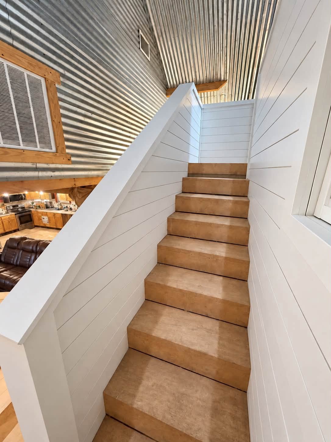 Wood staircase bordered by white horizontal paneling beside corrugated metal walls.
