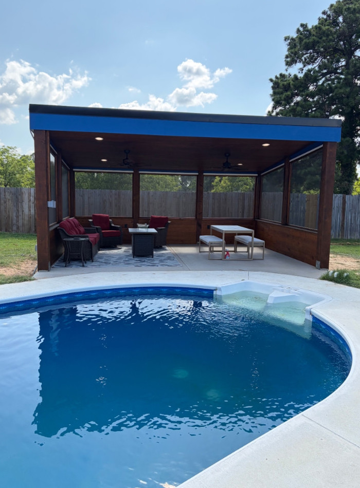 Covered patio with seating and a picnic table, viewed across a swimming pool.