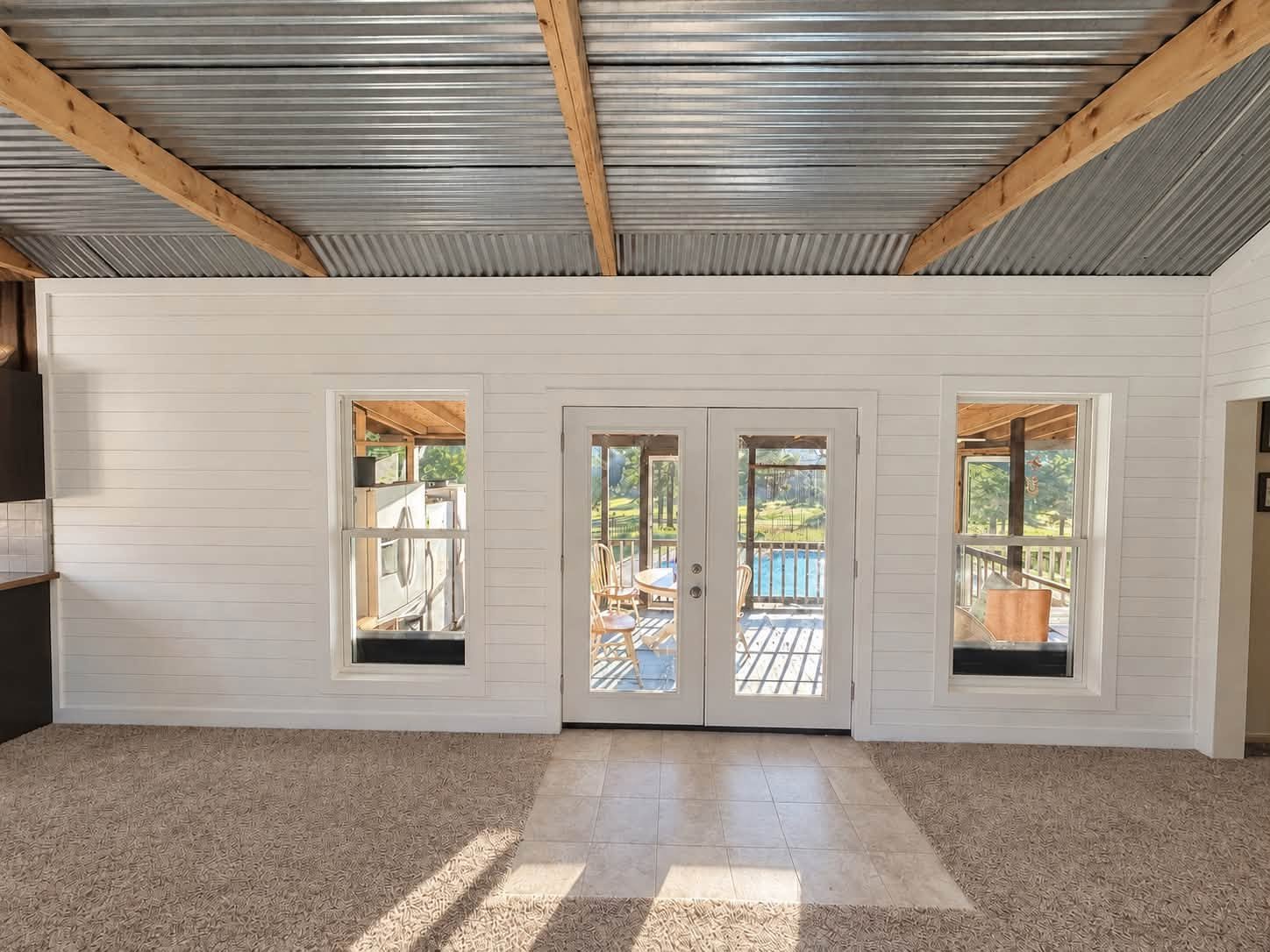 White-paneled room with glazed double doors, exposed wood beams and a corrugated metal ceiling.